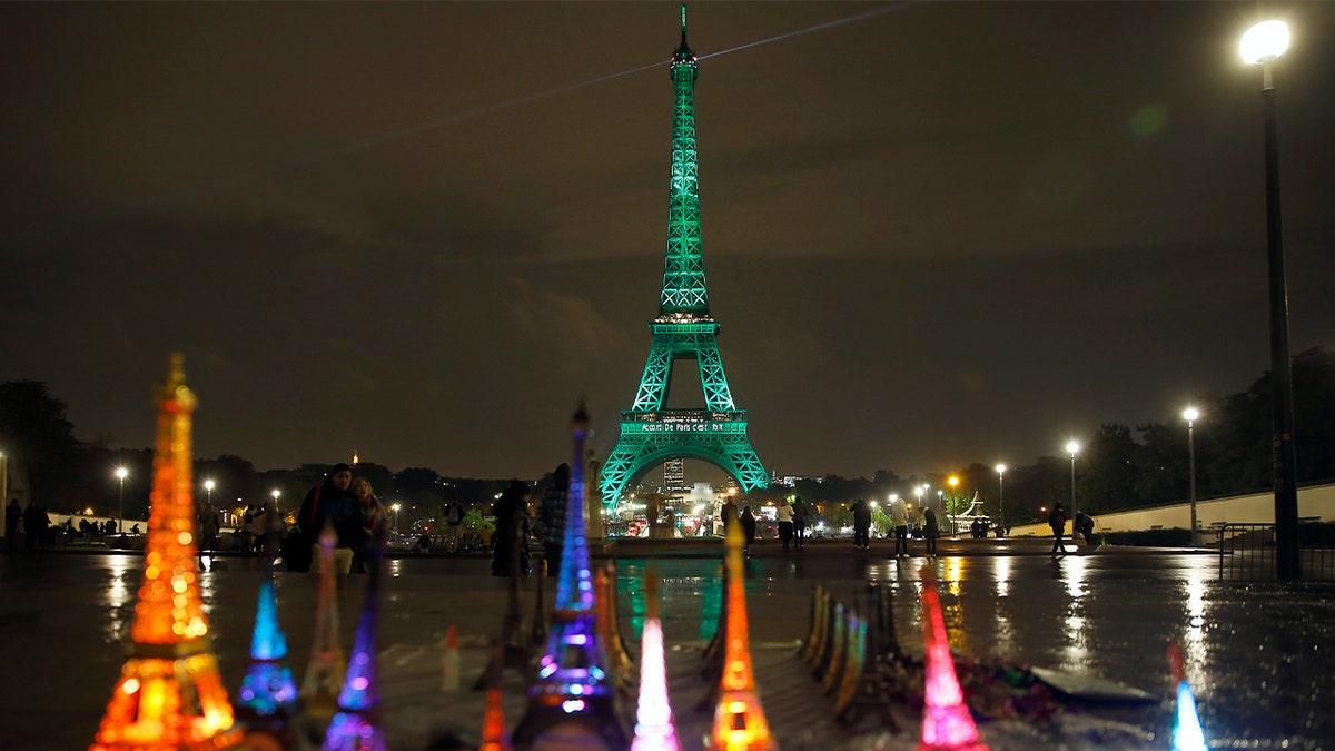 Small gift-size Eiffel Towers are seen in front of the Eiffel Tower illuminated in green with the words "Paris Agreement is Done" on Nov. 4, 2016, in Paris. Several Parisian monuments were illuminated in green to celebrate the first day of the application of the Paris COP21 climate accord.