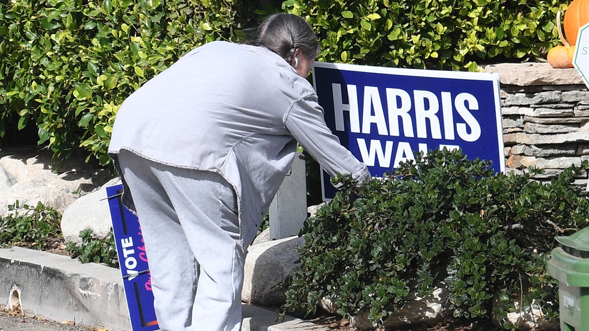 Sally Field with her back to the camera pulls out a Harris-Walz sign