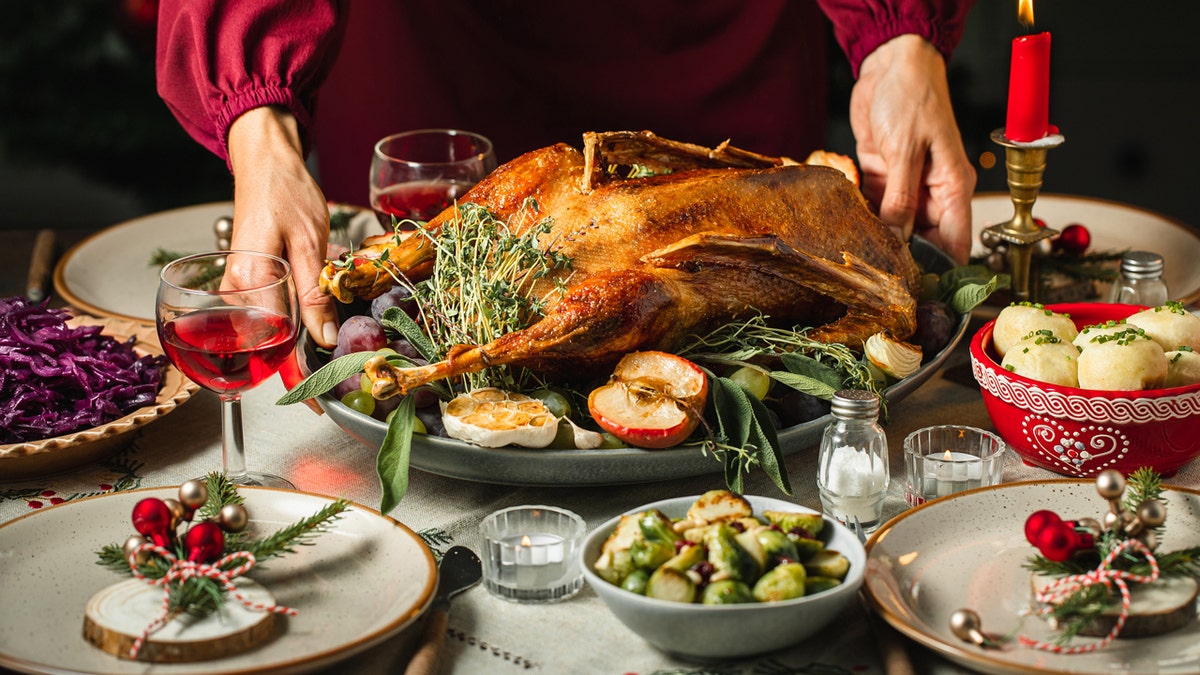 Close-up of woman's hands preparing the table, roast duck being served for Christmas dinner.