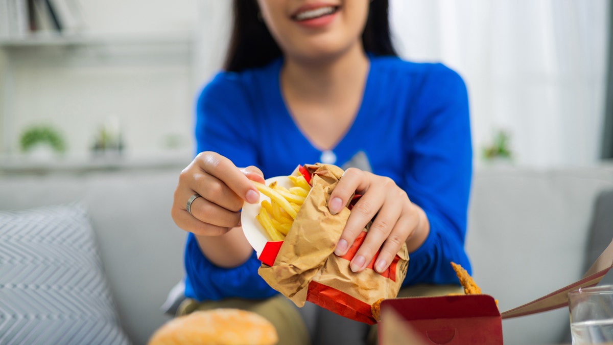 A woman smiles as she carries fried food in a bag.