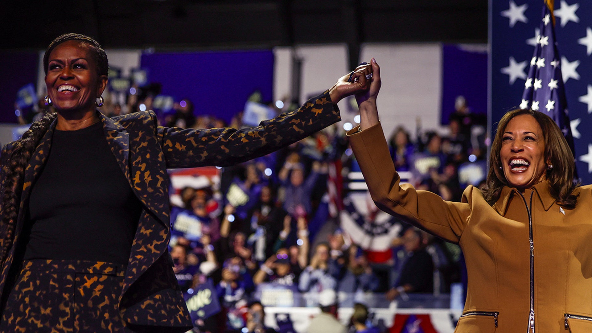 Democratic presidential nominee Vice President Kamala Harris and Former first lady Michelle Obama hold hands as they attend a campaign event for Harris at Wings Event Center