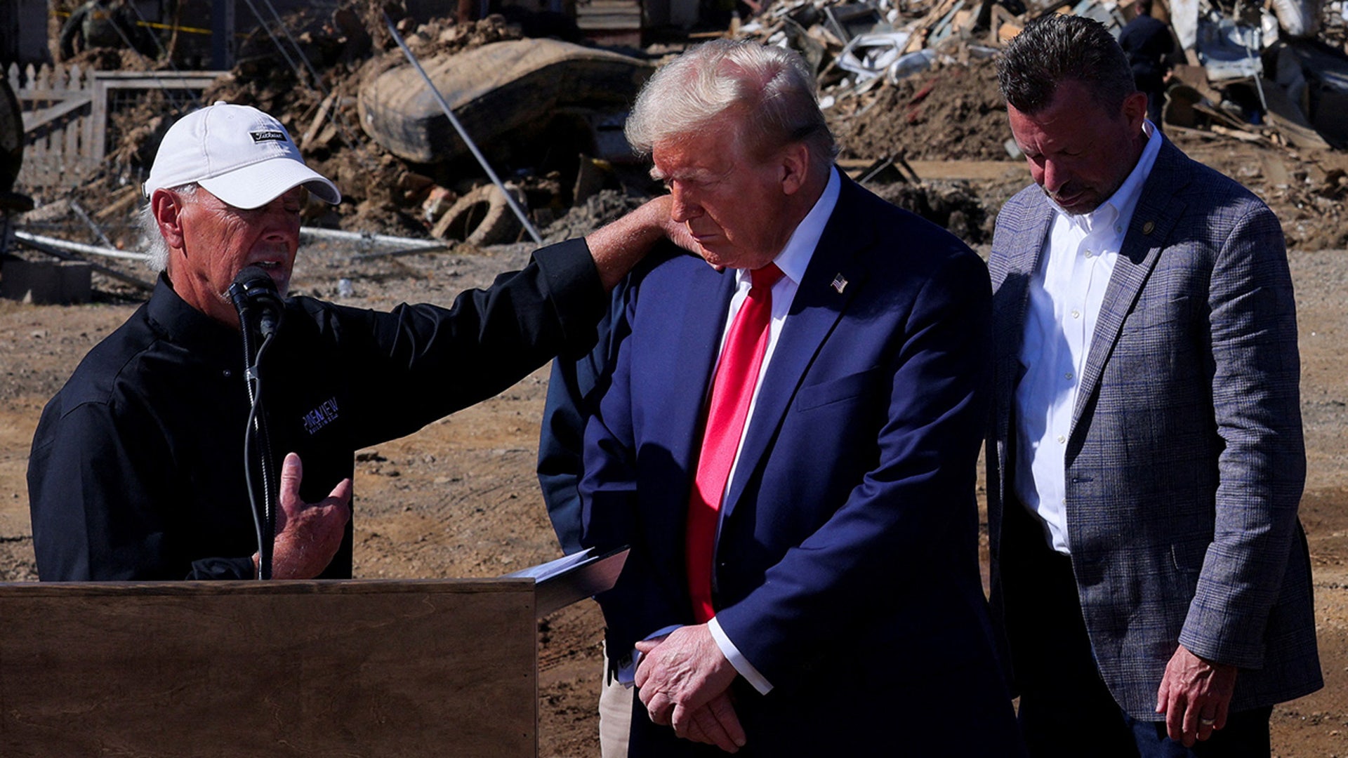 Republican presidential nominee and former President Donald Trump prays with Mike Stewart as he visits a site damaged by Hurricane Helene