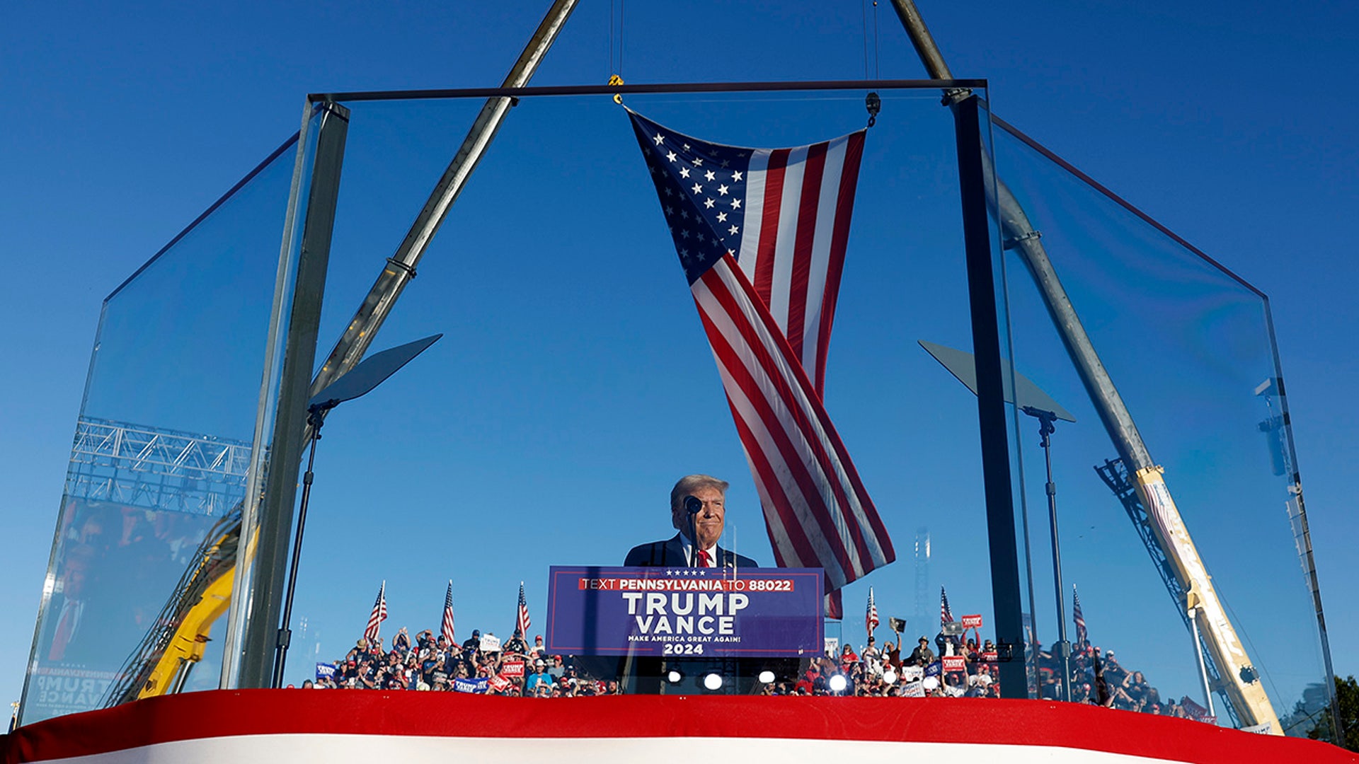 Republican presidential nominee and former President Donald Trump addresses a campaign rally from behind bullet resistant glass at the Butler Farm Show