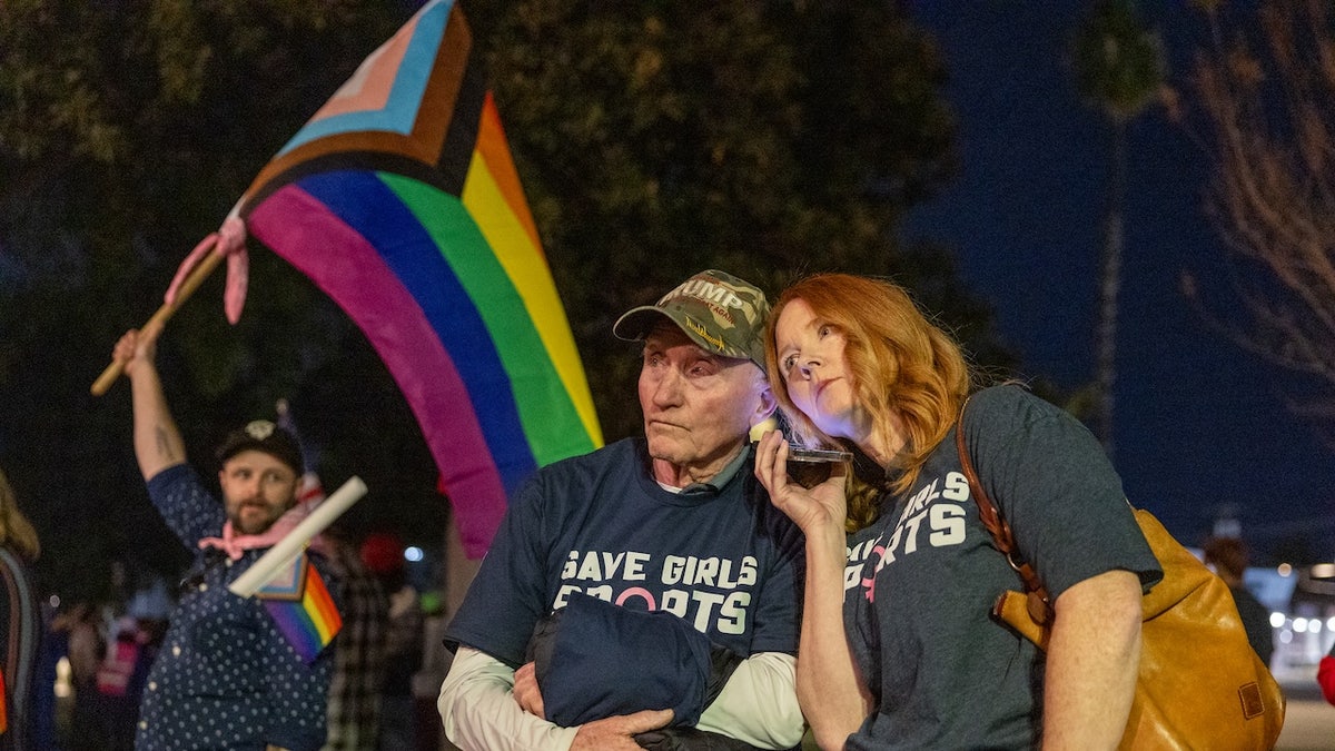 Transgender athlete supporter Kyle Harp, left, of Riverside holds the progress pride flag as "Save Girls Sports" supporters Lori Lopez and her dad, Pete Pickering, both of Riverside, listen to a debate outside a Riverside Unified School District meeting Dec. 19, 2024. 