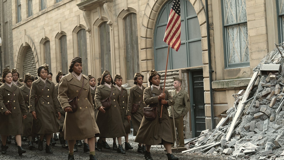 The 6888th Postal Battalion marches down a street in a scene from Netflix "The six triple eights." Woman in the foreground holding an American flag.