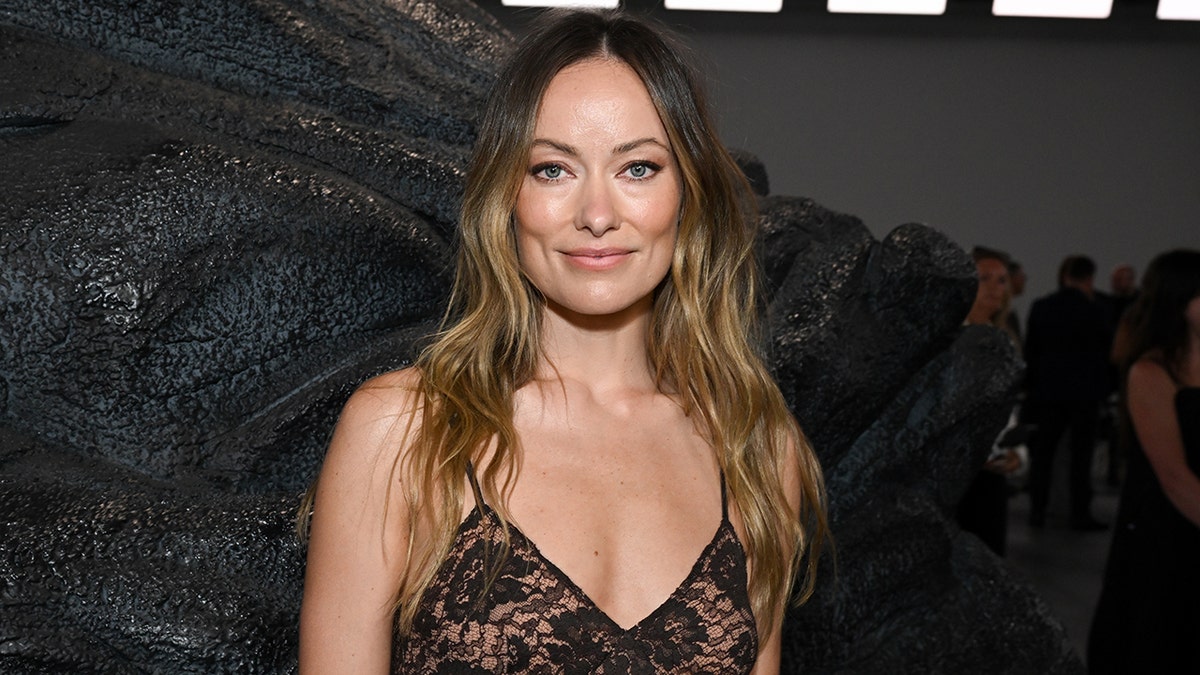 Olivia Wilde soft smiles in a black lacy v-neck dress