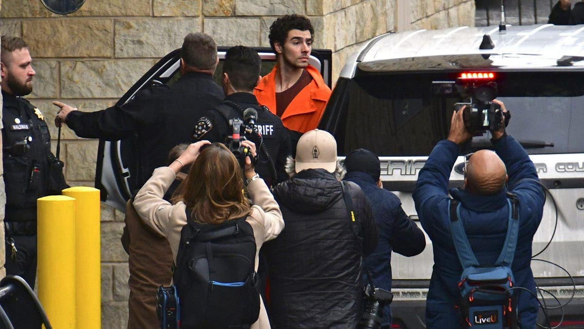 Photographers swarm a police vehicle as Luigi Mangione is escorted into court wearing an orange jail jumpsuit