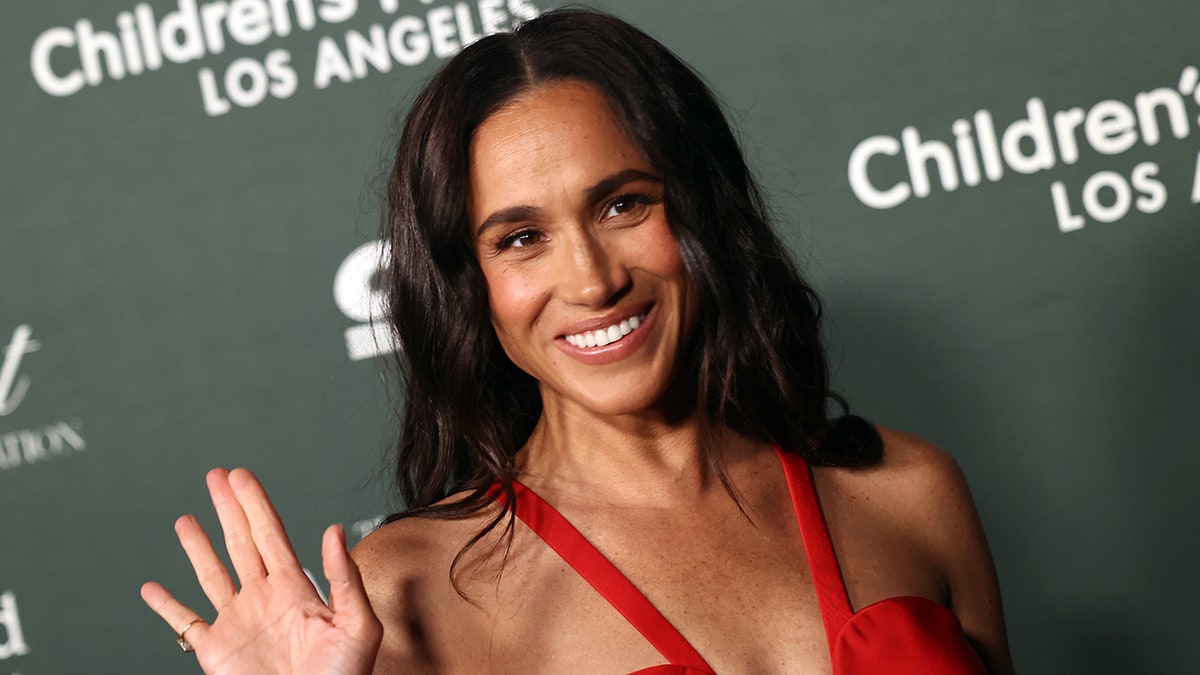 Meghan Markle waving and wearing a strappy red dress