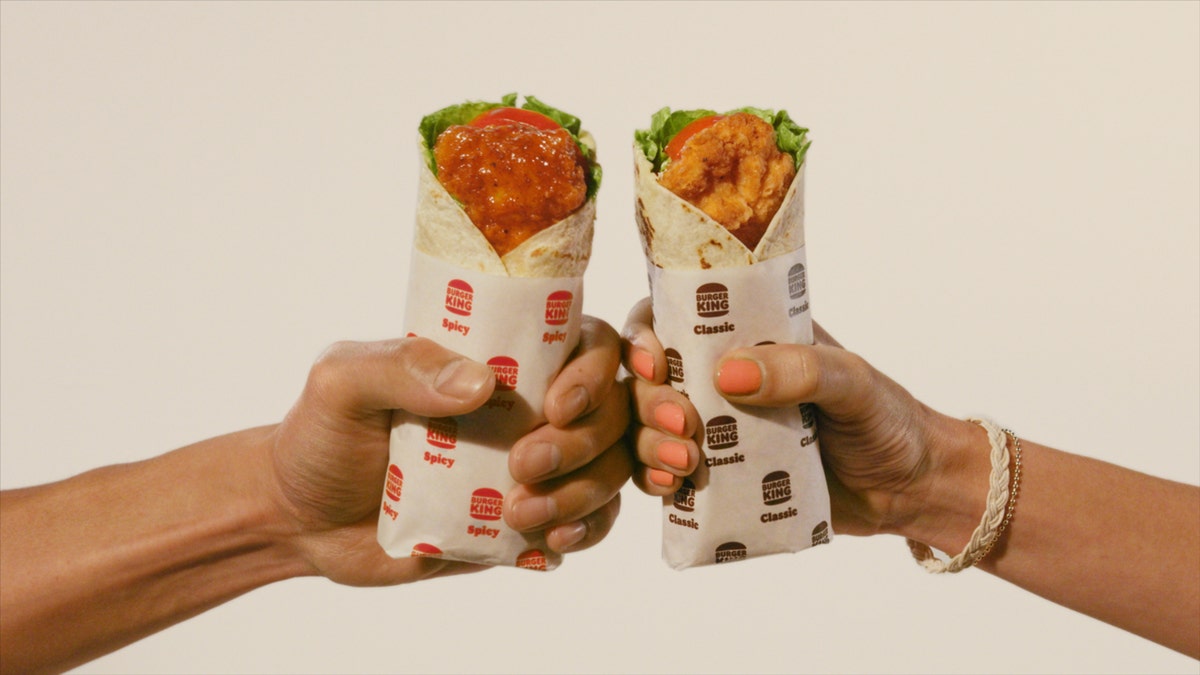A man's hand holds a spicy Royal Crispy Wrap, a woman's hand holds a classic Royal Crispy Wrap from Burger King.