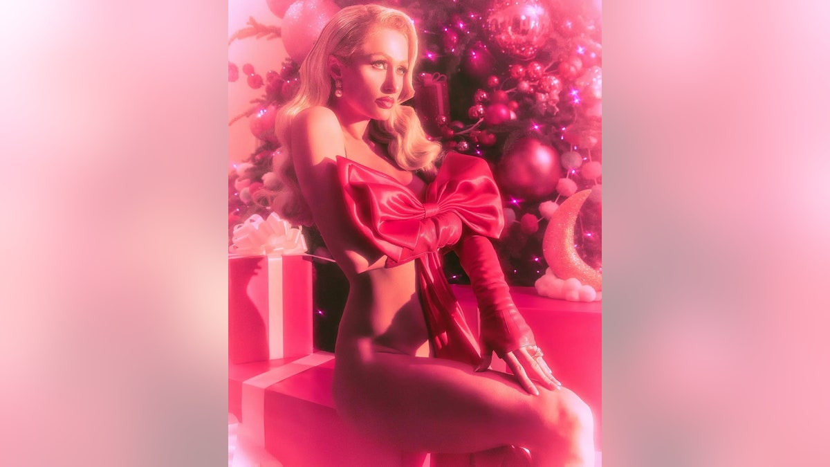 Paris Hilton sitting on top of a present and posing with a giant bow.