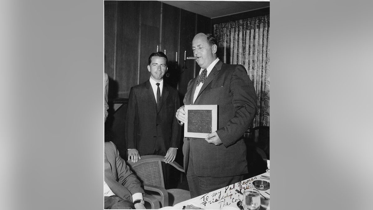 Norman Brokaw stands next to Colonel Tom Parker smoking a cigar