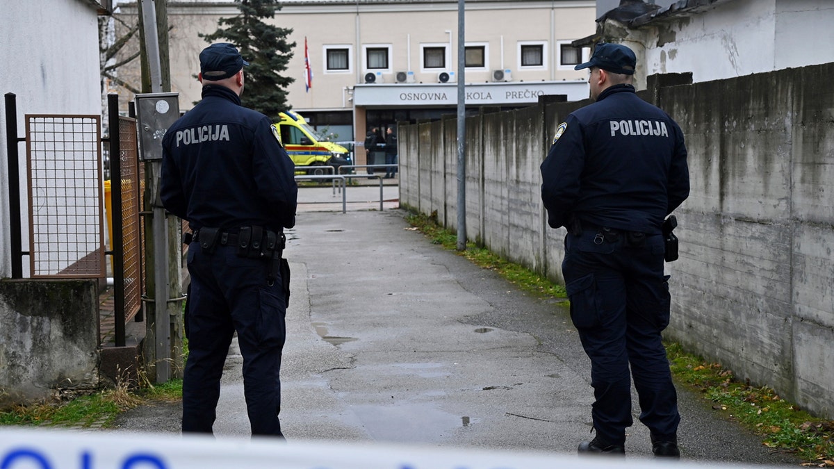 Two Croatian police officers stand guard outside of a school.