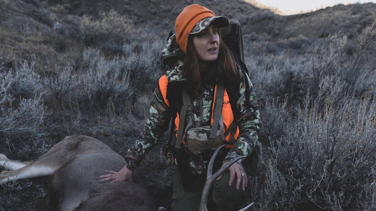 Danielle Prewett touches a dead mule deer while hunting.