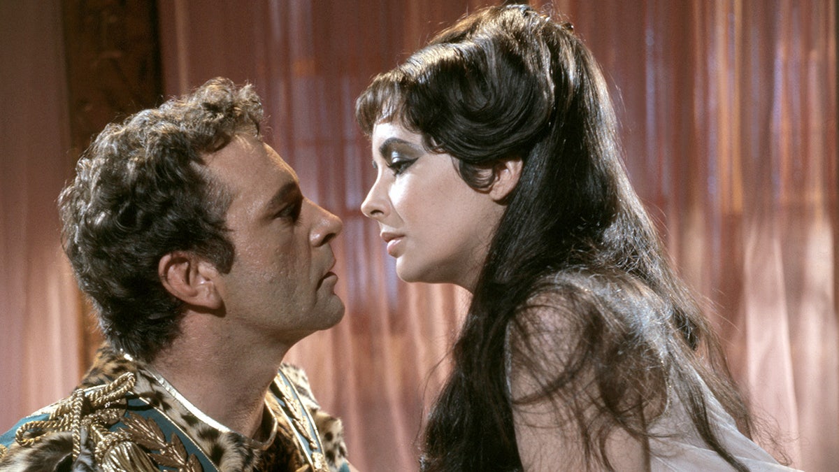 Richard Burton et Elizabeth Taylor en costume sur le point de s'embrasser.