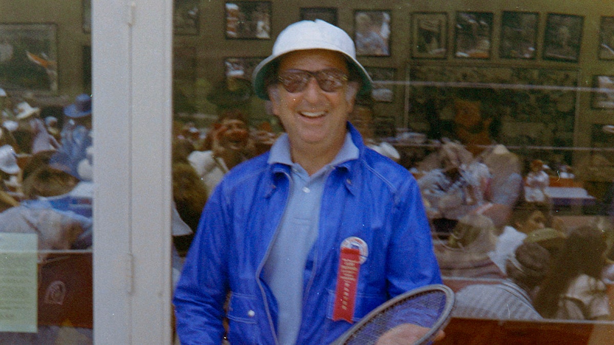 Jennings Lang dans une veste bleu vif et une chemise bleu pâle souriant