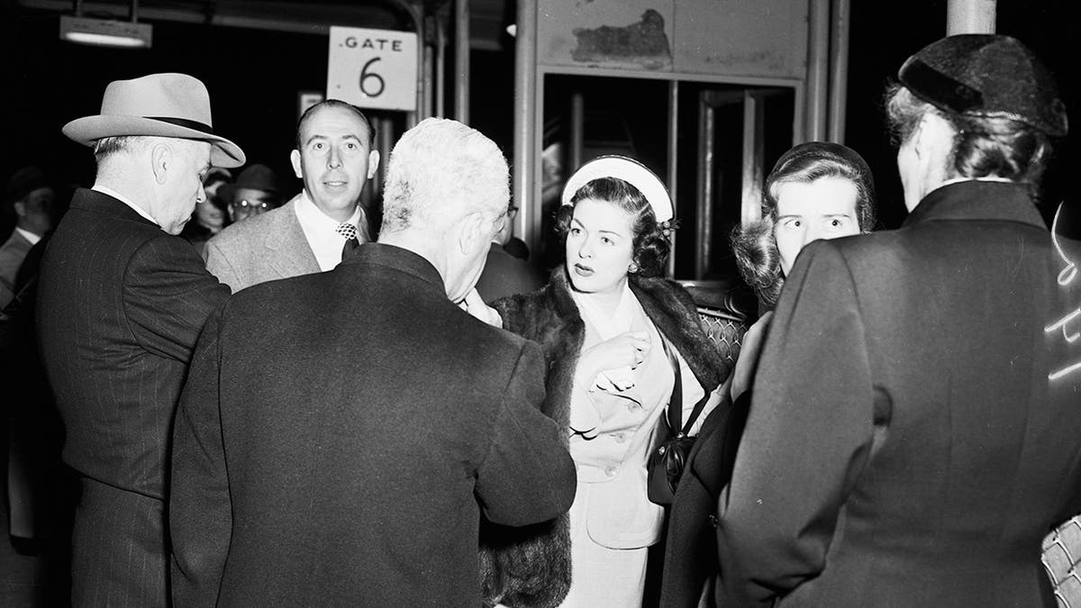 Joan Bennett entourée de photographes et de journalistes à l'air perplexe.