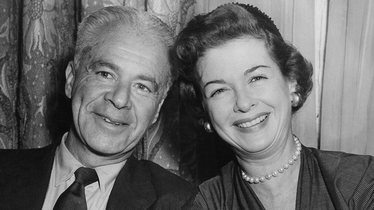 Un gros plan de Walter Wanger souriant avec Joan Bennett portant une robe et des perles.