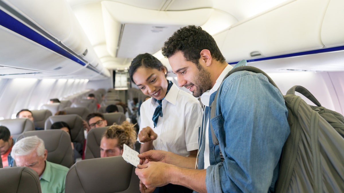 Flight attendant helps people find seats on the plane