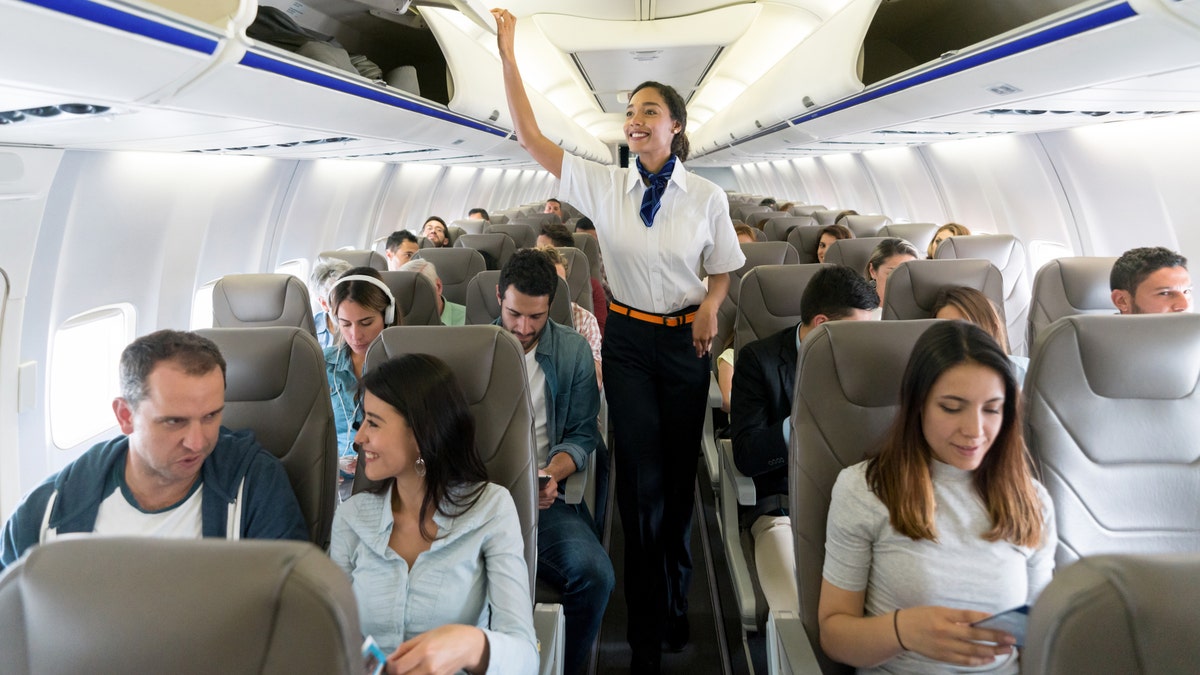 Airplane Ham Rirang Stewardess walking down the aisle in an airplane closing overhead compartments and smiling - Travel Concepts