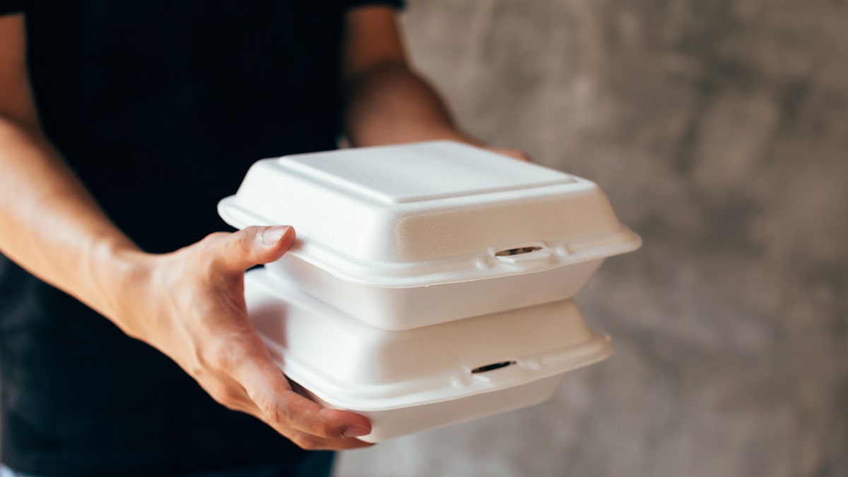 Close-up of delivery man handing a slack of foam lunch box.