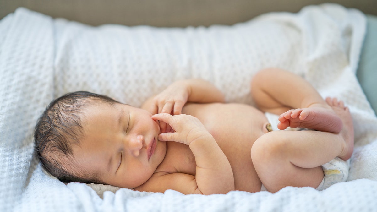 A newborn baby rests in his diaper in a cradle