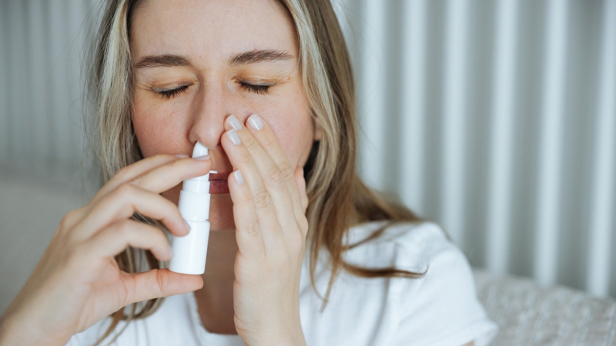 woman using a nasal spray in her bedroom