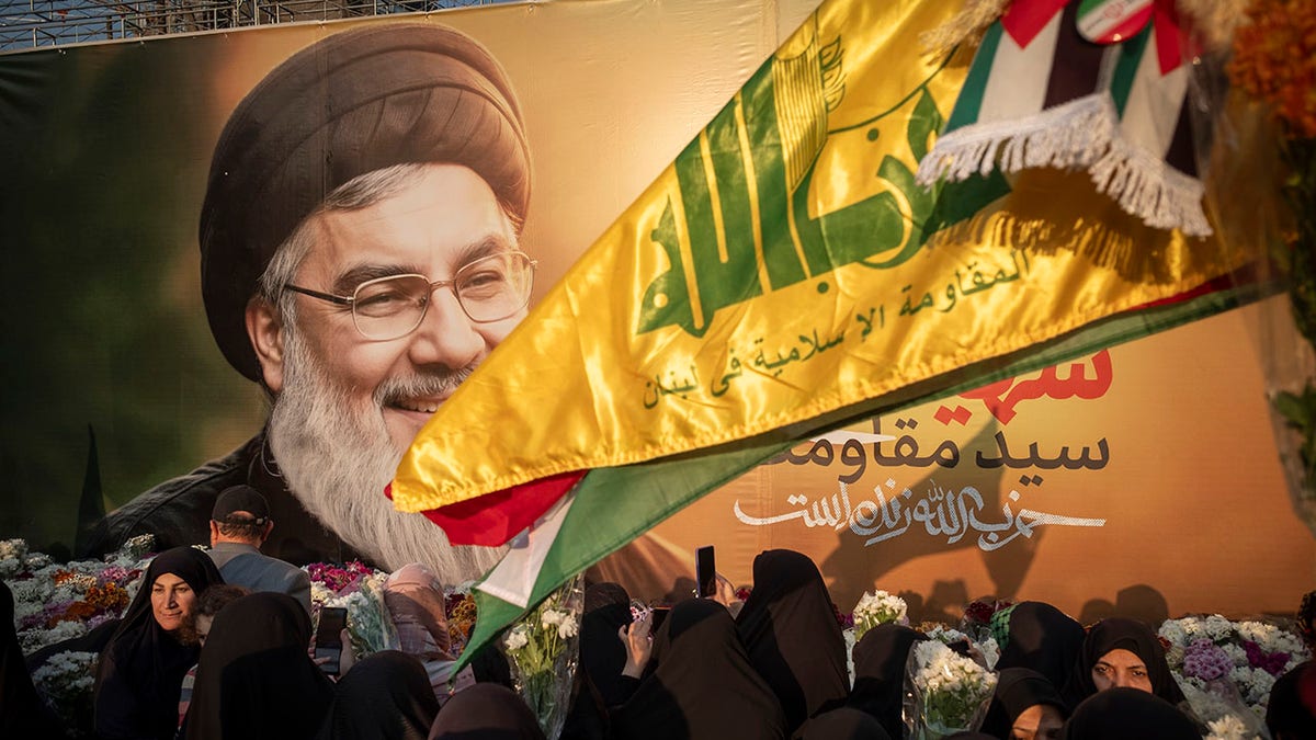 Pengunjuk rasa Iran membawa bunga sambil berdiri di depan spanduk raksasa yang menggambarkan potret Sekretaris Jenderal Hizbullah Lebanon, Hassan Nasrallah, selama demonstrasi mengutuk serangan udara Israel terhadap markas besar Hizbullah di pinggiran kota Beirut, dan pembunuhan Hassan Nasrallah dan seorang komandan Pasukan Quds Korps Pengawal Revolusi Islam (IRGC), Jenderal Abbas Nilforoushan, di Teheran, Iran, pada 30 September 2024. 