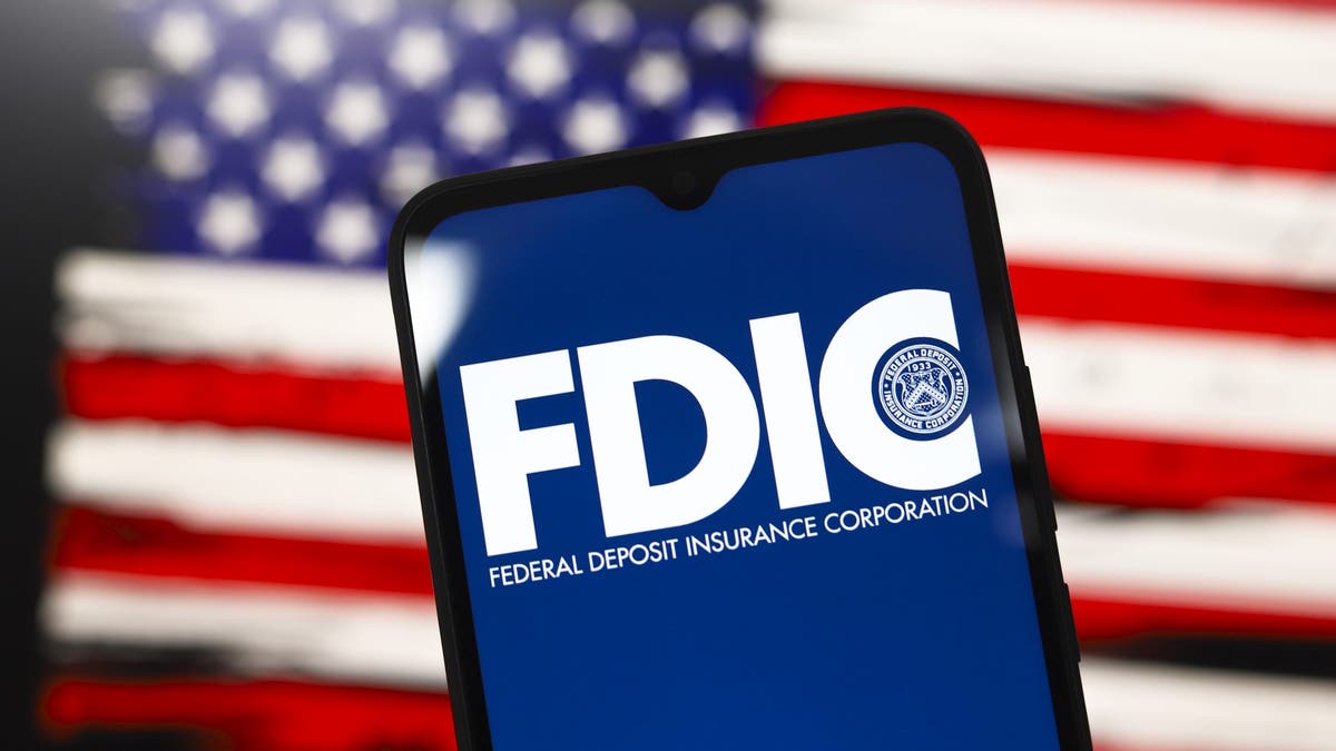 The United States Federal Deposit Insurance Corporation (FDIC) logo appears on the screen of a smartphone, and in the background, the flag of the United States is on the computer screen in Reno, Nevada, on Dec. 3, 2024. 