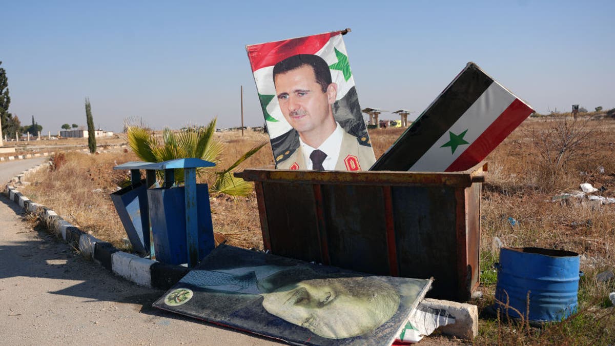 Topshot - Photo taken on December 3, 2024 at the entrance to the Khweiris military airfield in eastern Aleppo province shows a portrait of Syrian President Bashar al-Assad and the national flag on a garbage dump after the takeover of the area is shown. by rebel groups. The War Monitor on December 1 said that Ankara-backed groups had seized control of the towns of Sakhre and Qanassar, southeast of Aleppo, from government forces and also appeared at the Kweilis military airport.