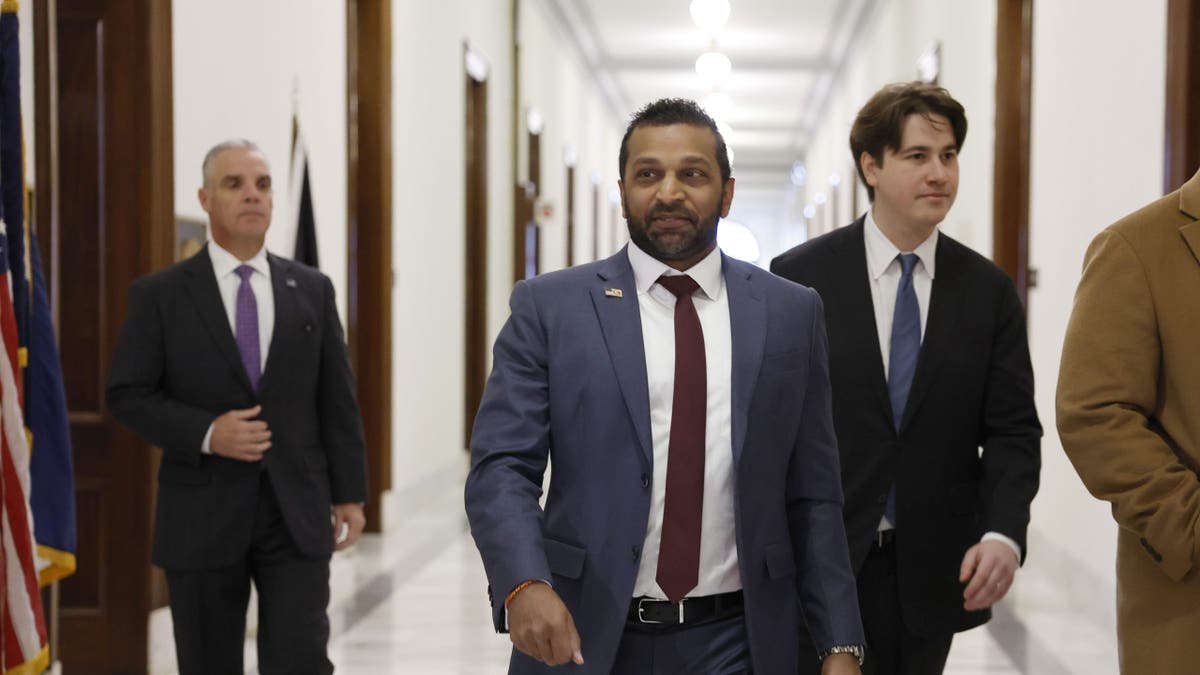 Kash Patel wearing a suit walking down a hallway