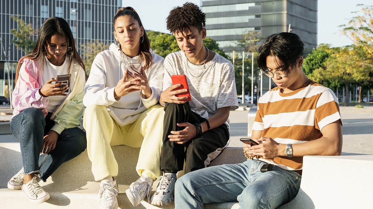 Group of teenage friends sitting together using their phones