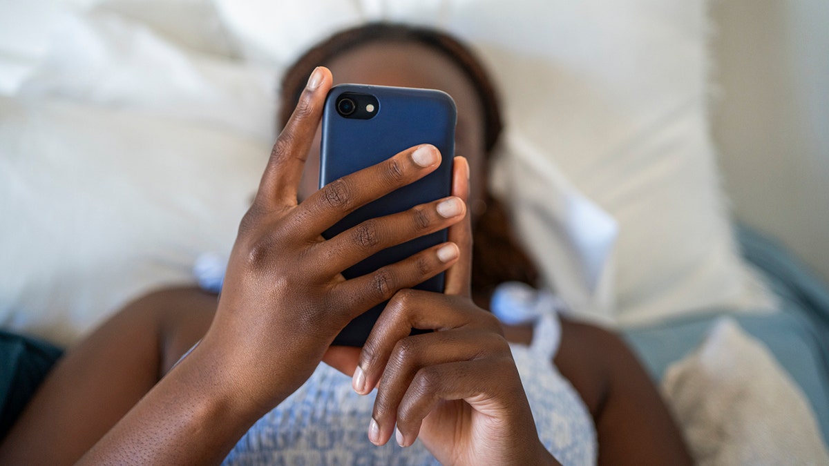 Close up of a little girl using a smart phone while sleeping alone in her bed at home