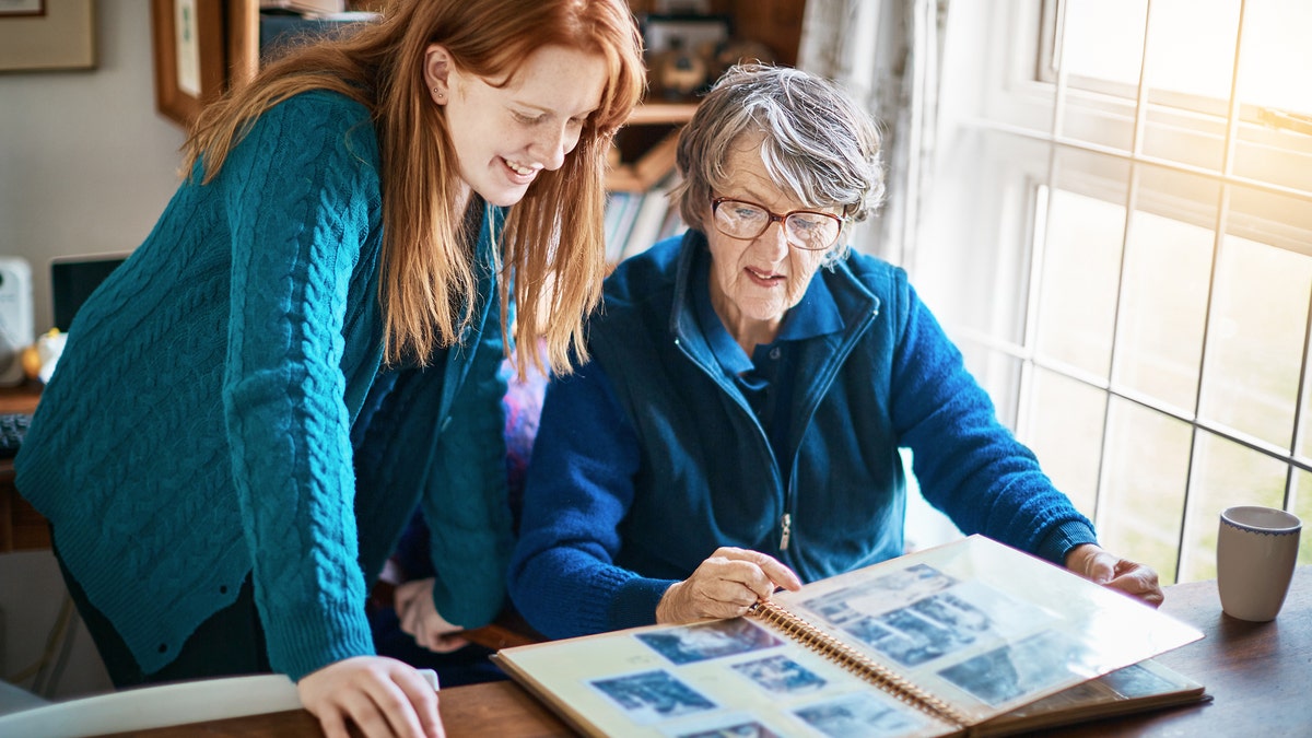 A happy young woman looks at family pictures in a photo album with her grandmother