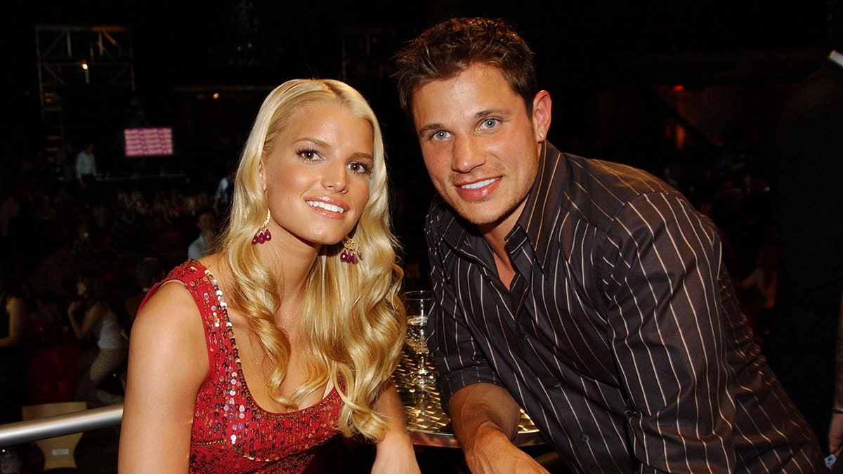 Jessica Simpson sonríe con un vestido rojo brillante junto a Nick Lachey con una sedosa camisa negra de rayas finas