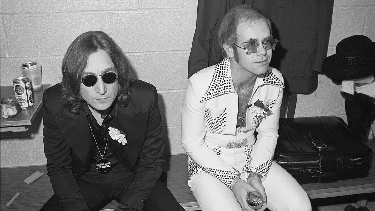 Black and white photo of John Lennon and Elton sitting together backstage