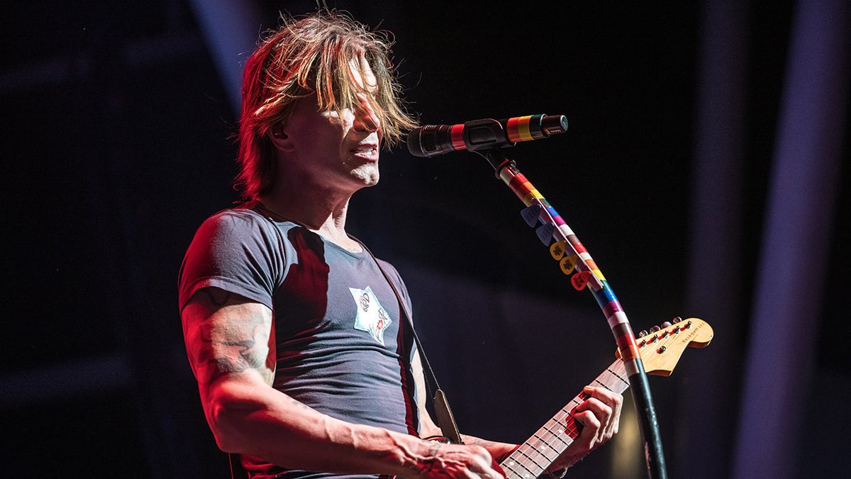 John Rzeznik canta delante de un micrófono mientras sostiene una guitarra.