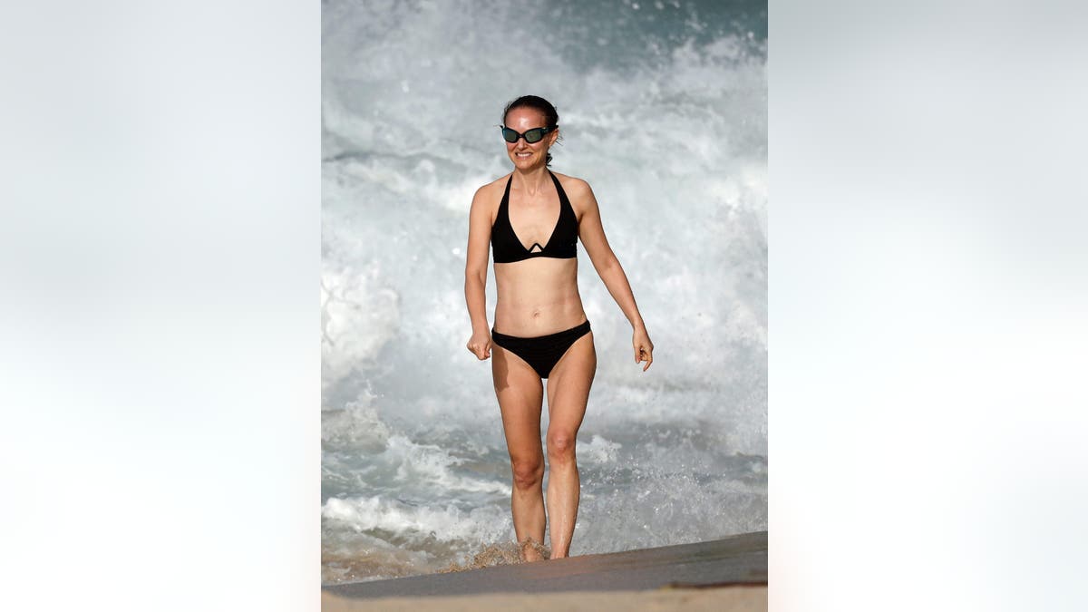 Natalie Portman in a black bikini walking on the beach