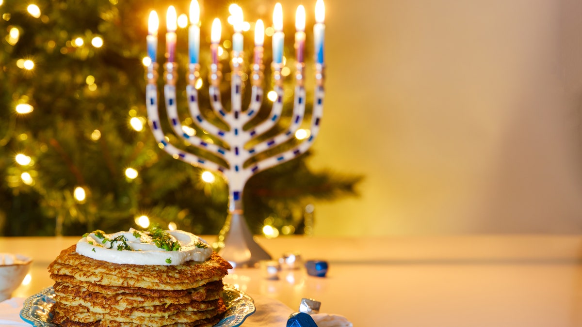 Jewish holiday dinner with Hanukkah menorah and crispy potato latkes and Christmas tree in background