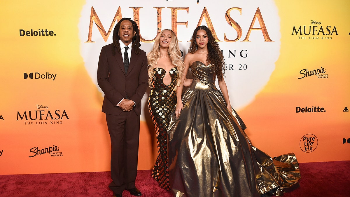 Jay-Z, de traje granate, con las manos bajo la cintura, junto a su esposa Beyoncé, con un vestido dorado de gran escote, y su hija Blue Ivy, con un vestido dorado sin tirantes, en el estreno de "Mufasa: El Rey León