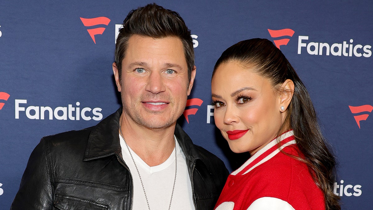 Nick Lachey con una chaqueta de cuero sonríe en la alfombra con su mujer Vanessa Lachey con una chaqueta letterman roja