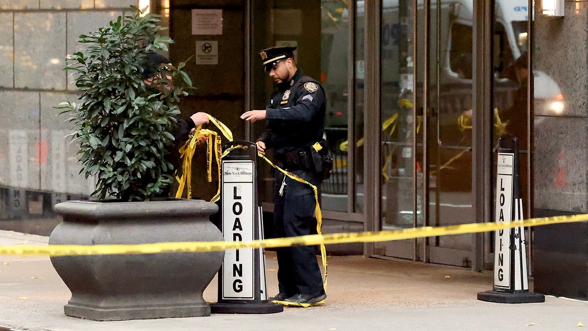 NYPD officer with yellow tape stands outside the Hilton hotel where Brian Thompson was murdered