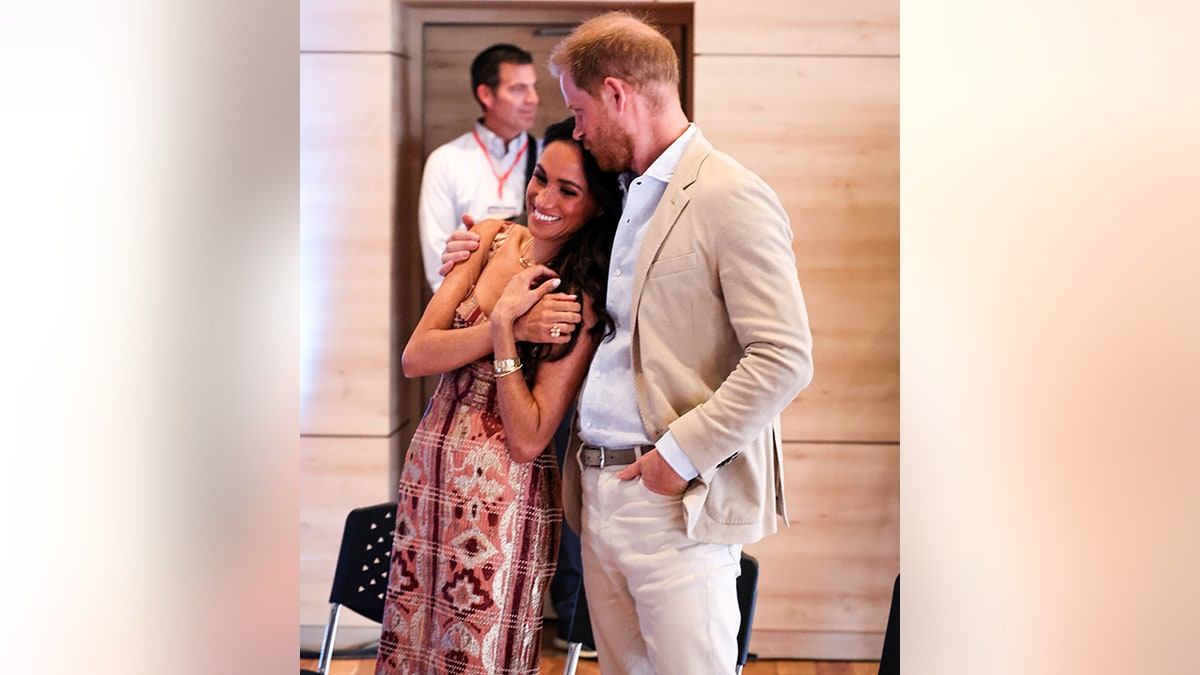 Meghan Markle crosses her arms and leans into Prince Harry who kisses her on top of her head