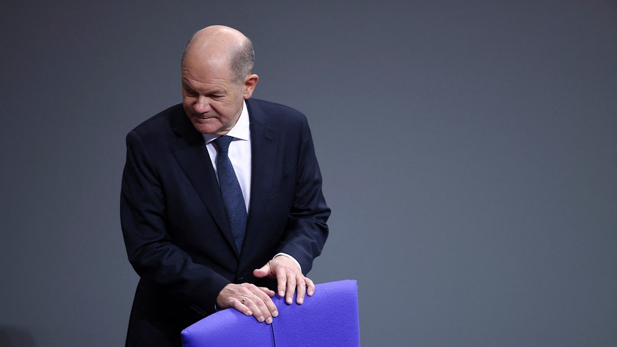 German Chancellor Olaf Scholz stands behind the chair