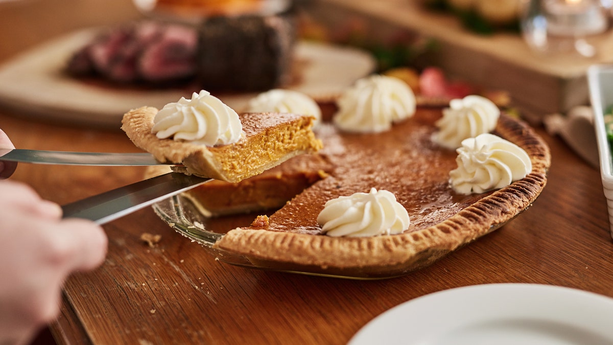 A piece of pumpkin pie is held by carving utensils on the dining room table of a home.