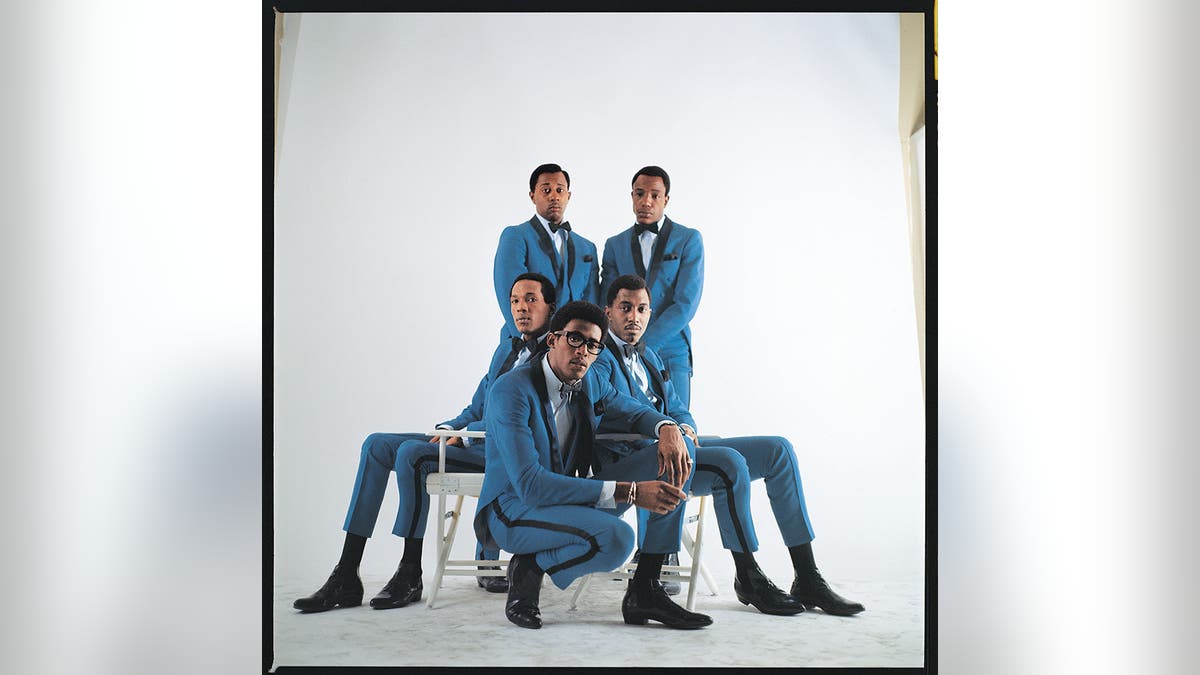 The Temptations posing and sitting next to each other in matching bright blue suits.