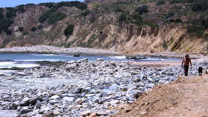 A‌ resident⁣ walks next to a rocky coastline in Palos Verdes. Human remains ​were discovered⁢ in the coastal city this week.