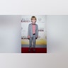 Hudson Meek in a grey two piece suit and red button down looks stoic as a child on the carpet