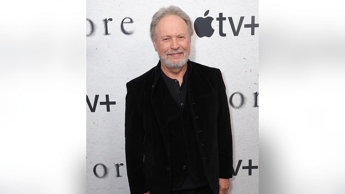 Billy Crystal in a black suit smooth smiles on the carpet