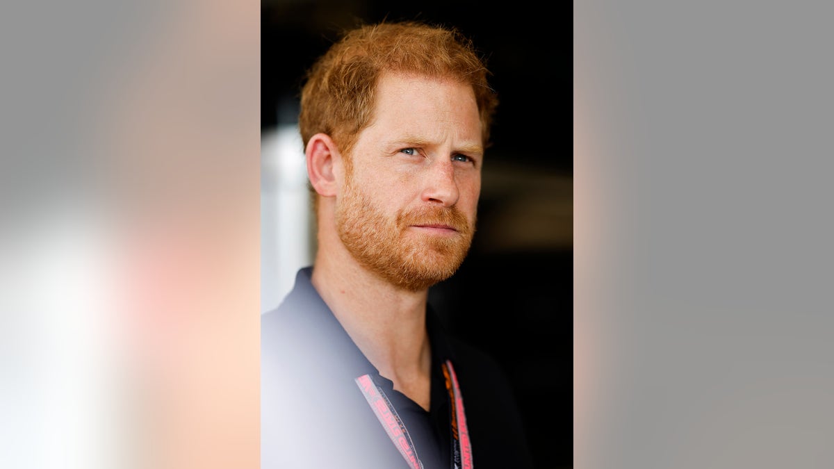 Un primer plano del príncipe Harry mirando hacia arriba con un polo azul marino.