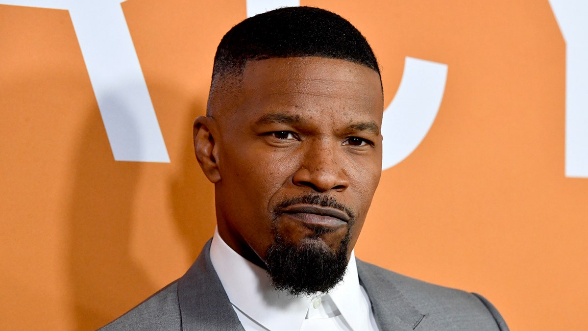 Jamie Foxx con un traje gris hace un serio mohín a la cámara en la alfombra